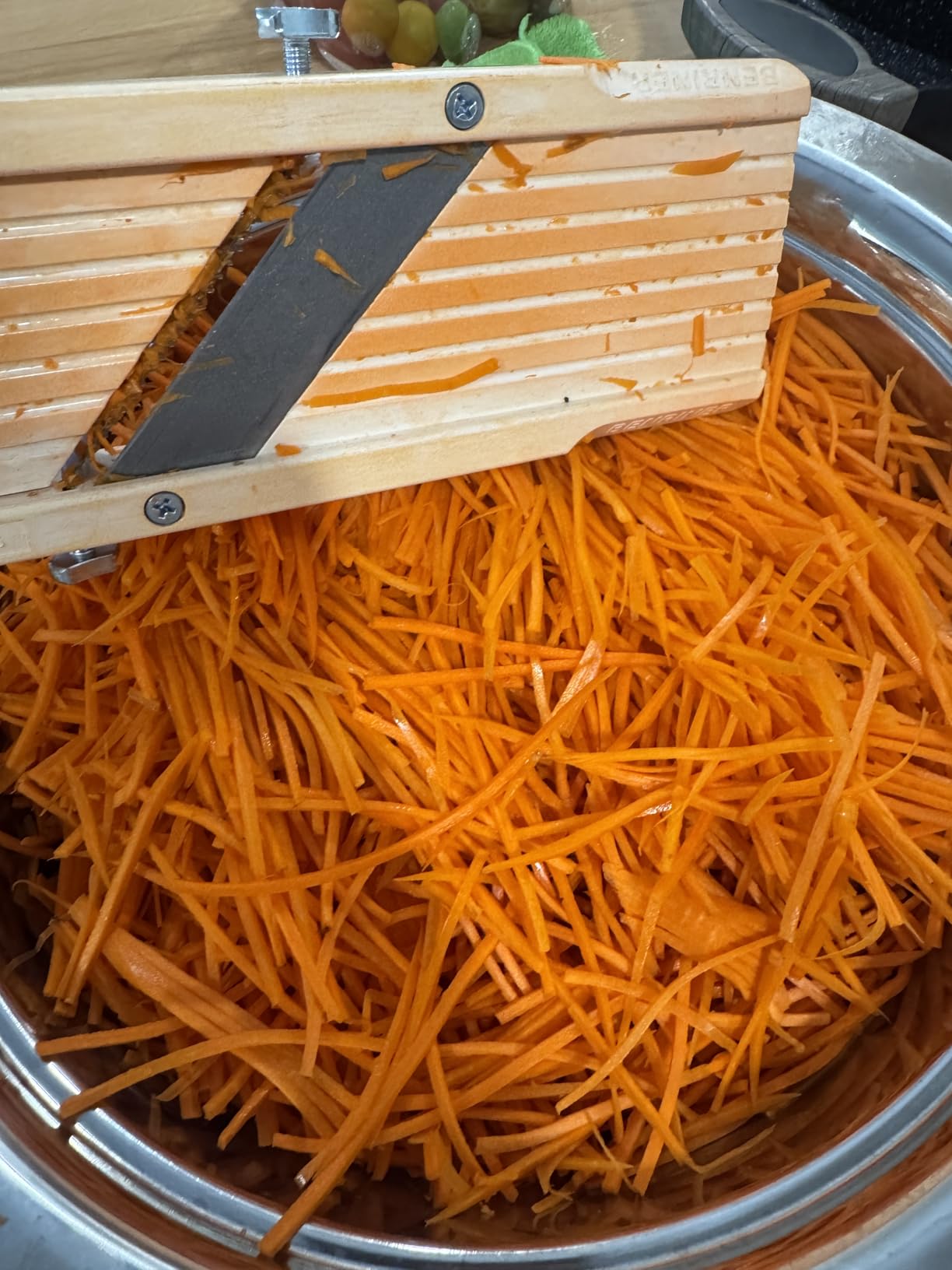 Benriner resting across a metal bowl filled with fine carrot julienne cut on a comb blade